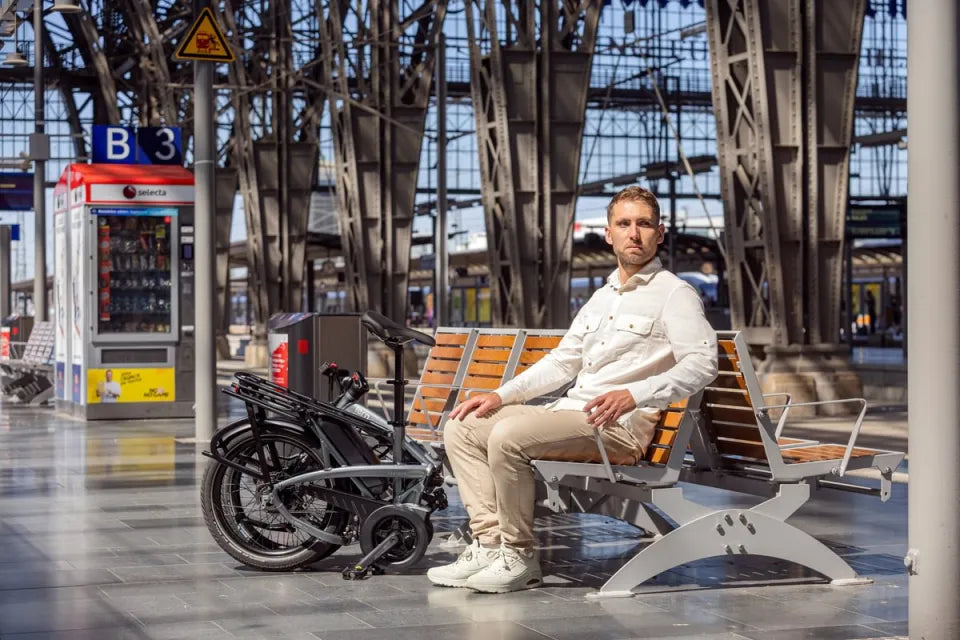 Man sitting on train station bench with Tern Vektron folding e-bike beside him