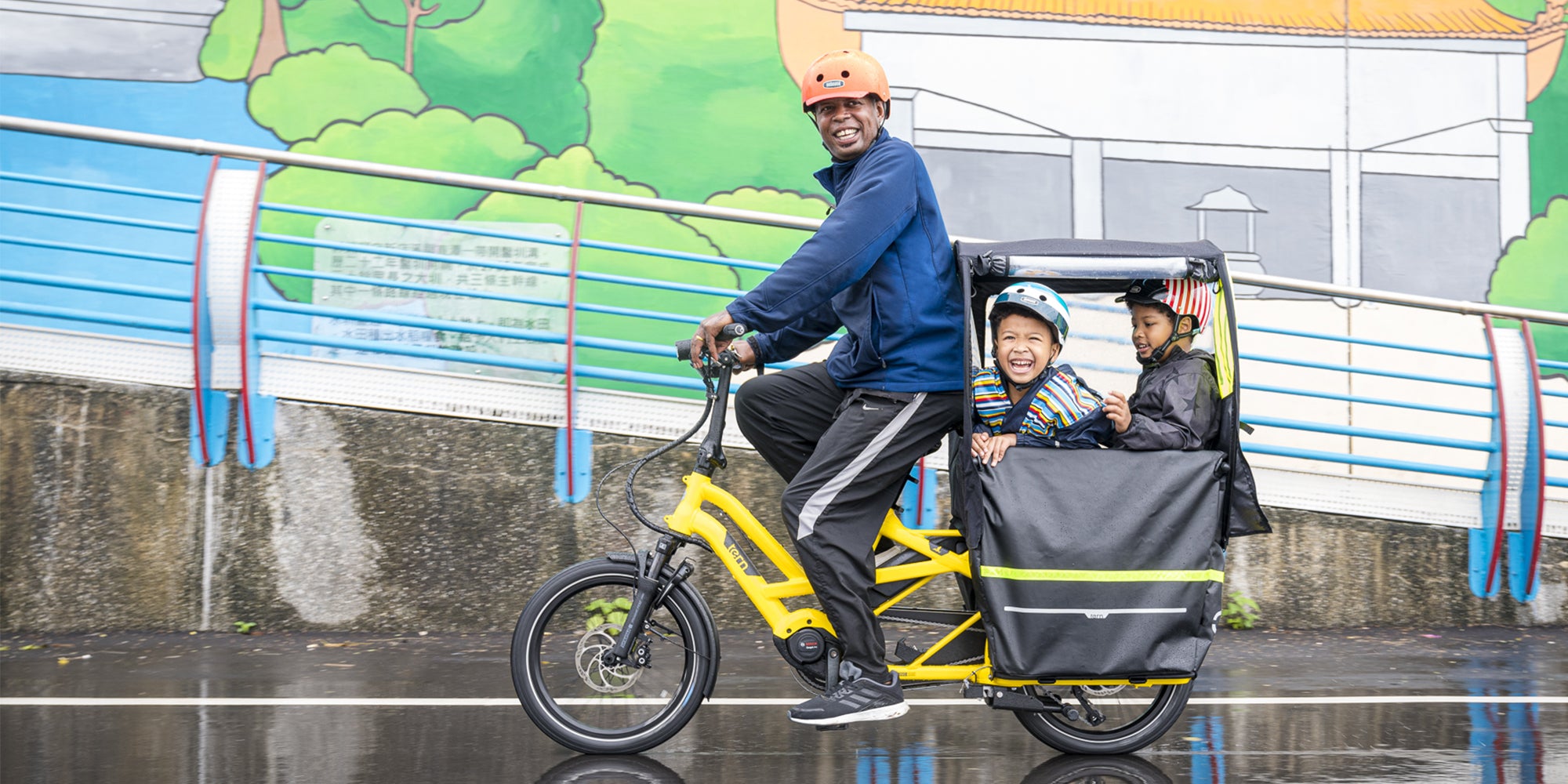 Man riding Tern GSD e-cargobike with two kids on back in covered compartment