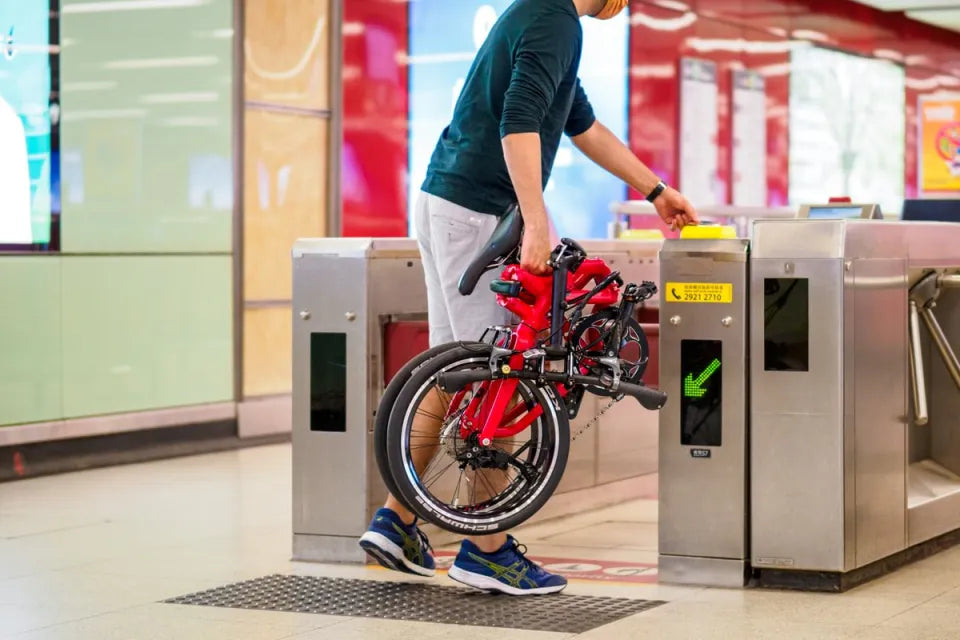 Man carrying Tern folding bike through public transportation station turnstile