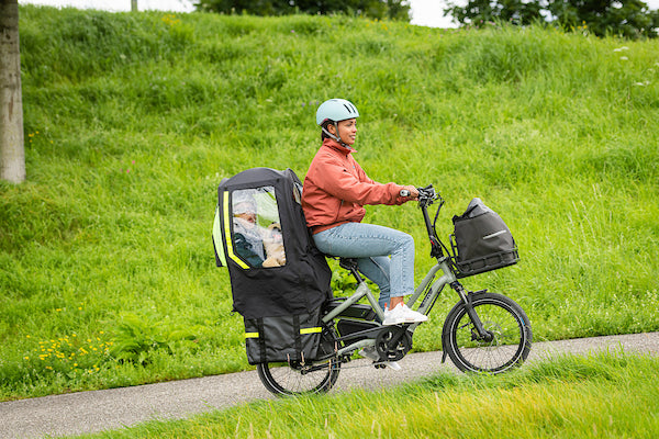 Woman riding Tern e-bike with child on the back under a protective cover