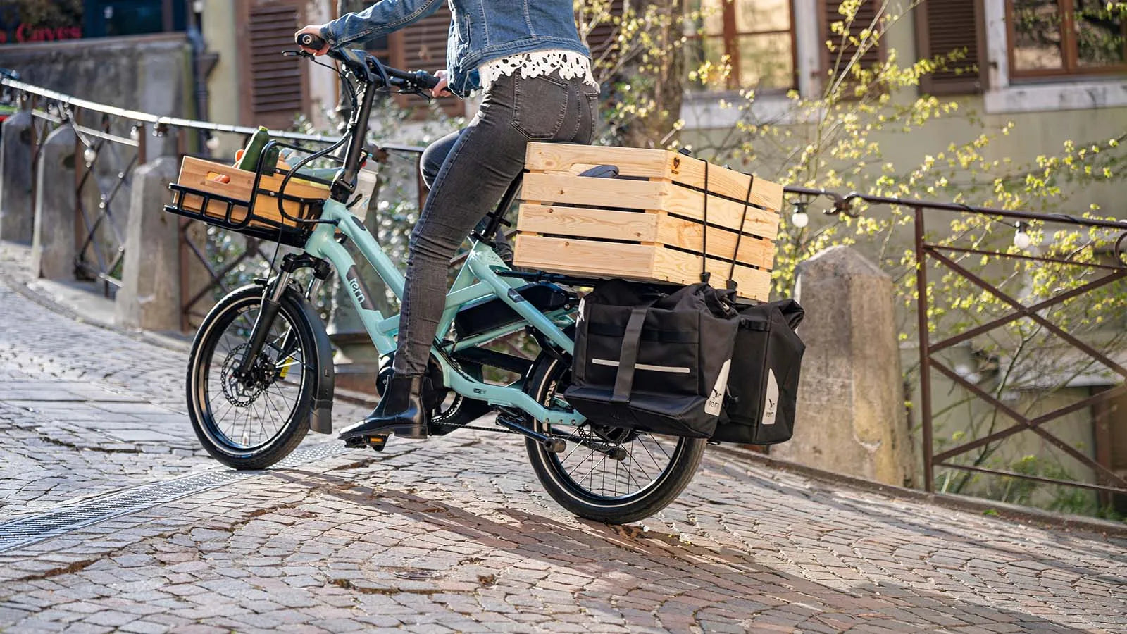 Woman riding Tern HSD cargo e-bike up cobblestone street