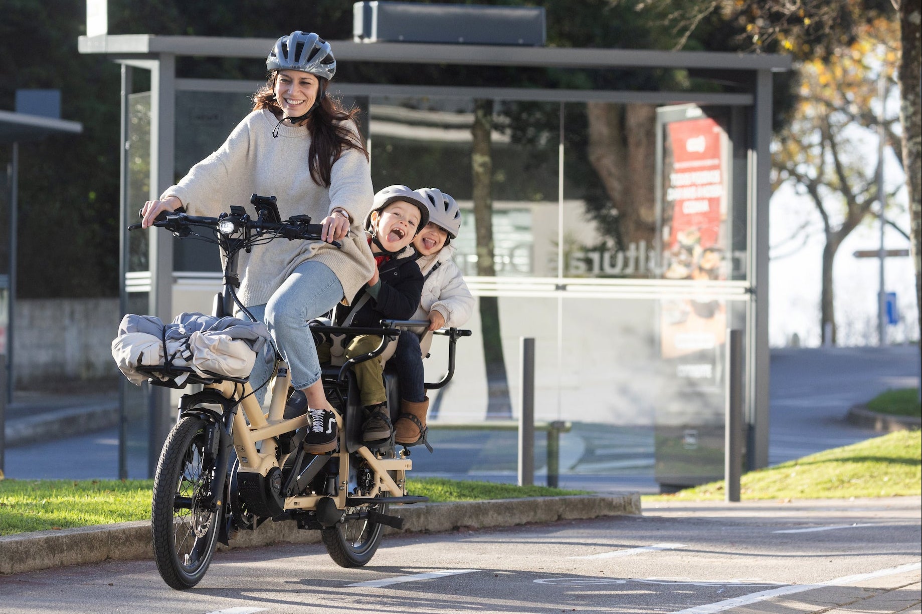 Woman riding a motorized Tern GSD Gen 3 electric cargo bike with two children in a city setting.