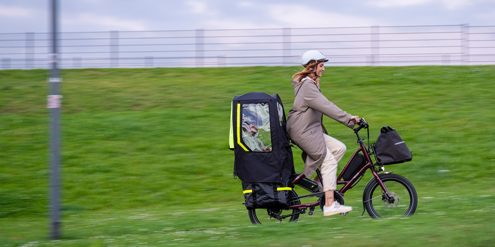 Woman riding Tern Quick Haul e-bike with child on the back in covered accessory
